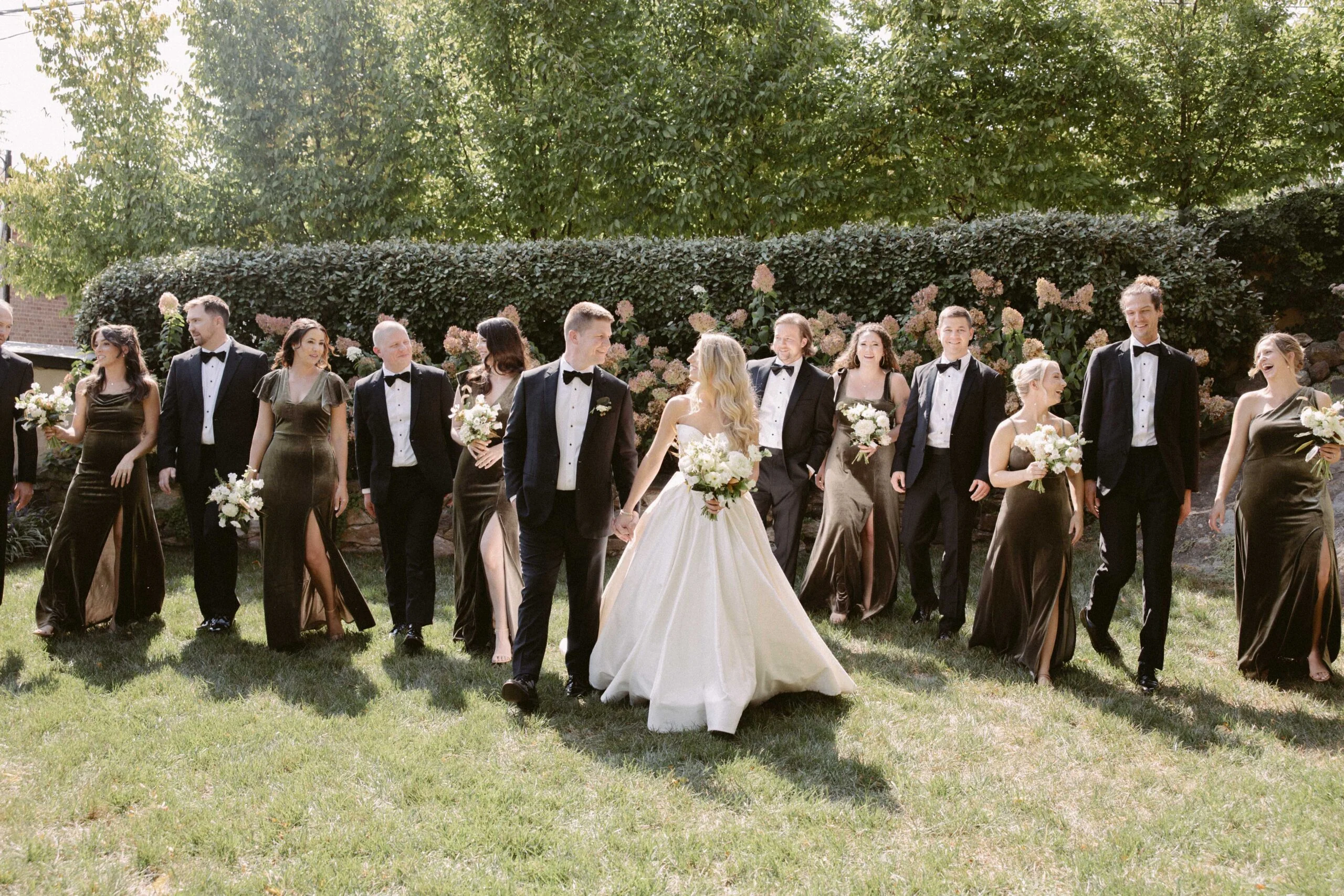 Wedding party walking in garden with lush greenery and blooming flowers.
