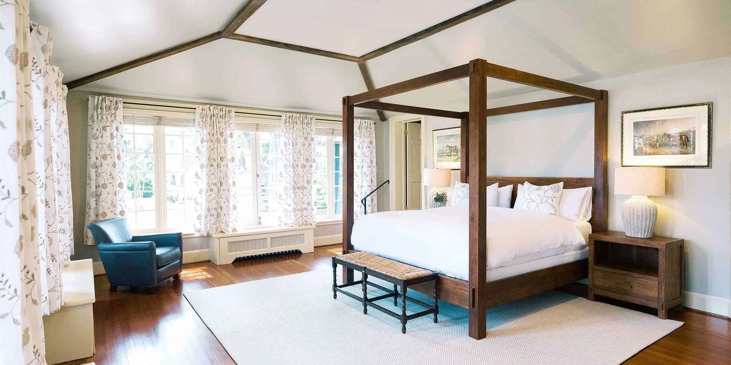 Cozy hotel room featuring a four-poster bed, elegant decor, and natural light from large windows.