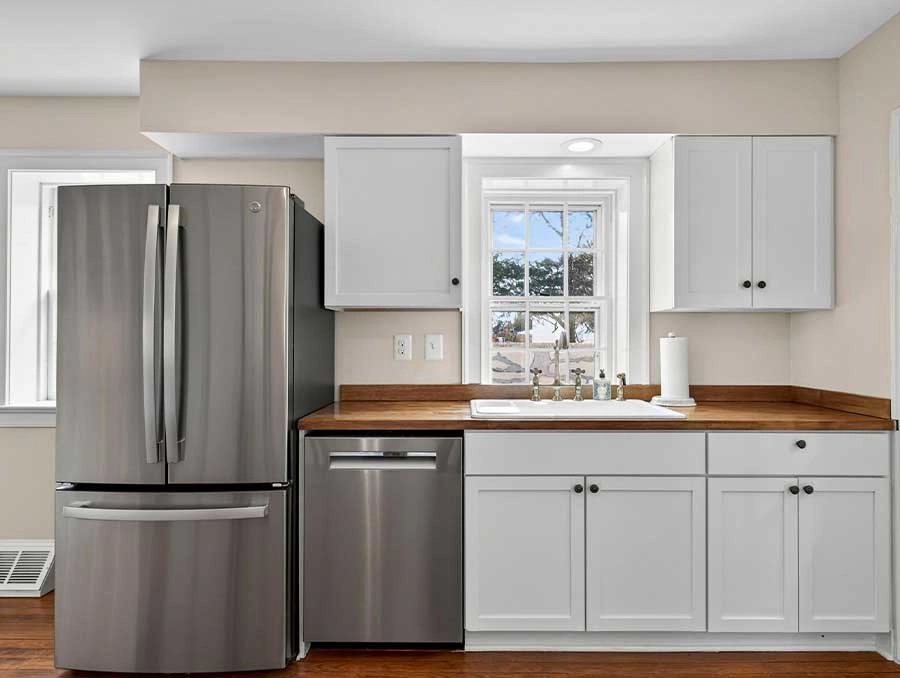 Modern kitchen featuring stainless steel refrigerator, dishwasher, and white cabinetry.