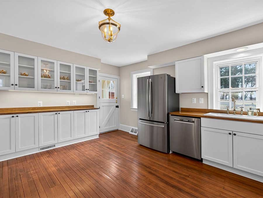 Bright, spacious kitchen featuring white cabinetry, a stainless steel refrigerator, and hardwood flo.