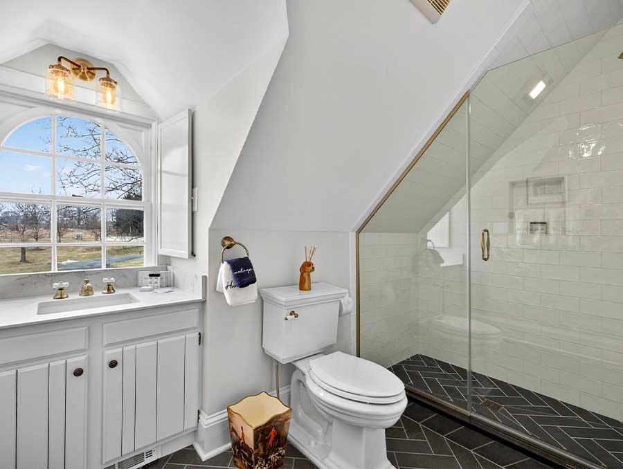 Bright bathroom featuring a white vanity, large window, and walk-in shower with glass enclosure. Per.